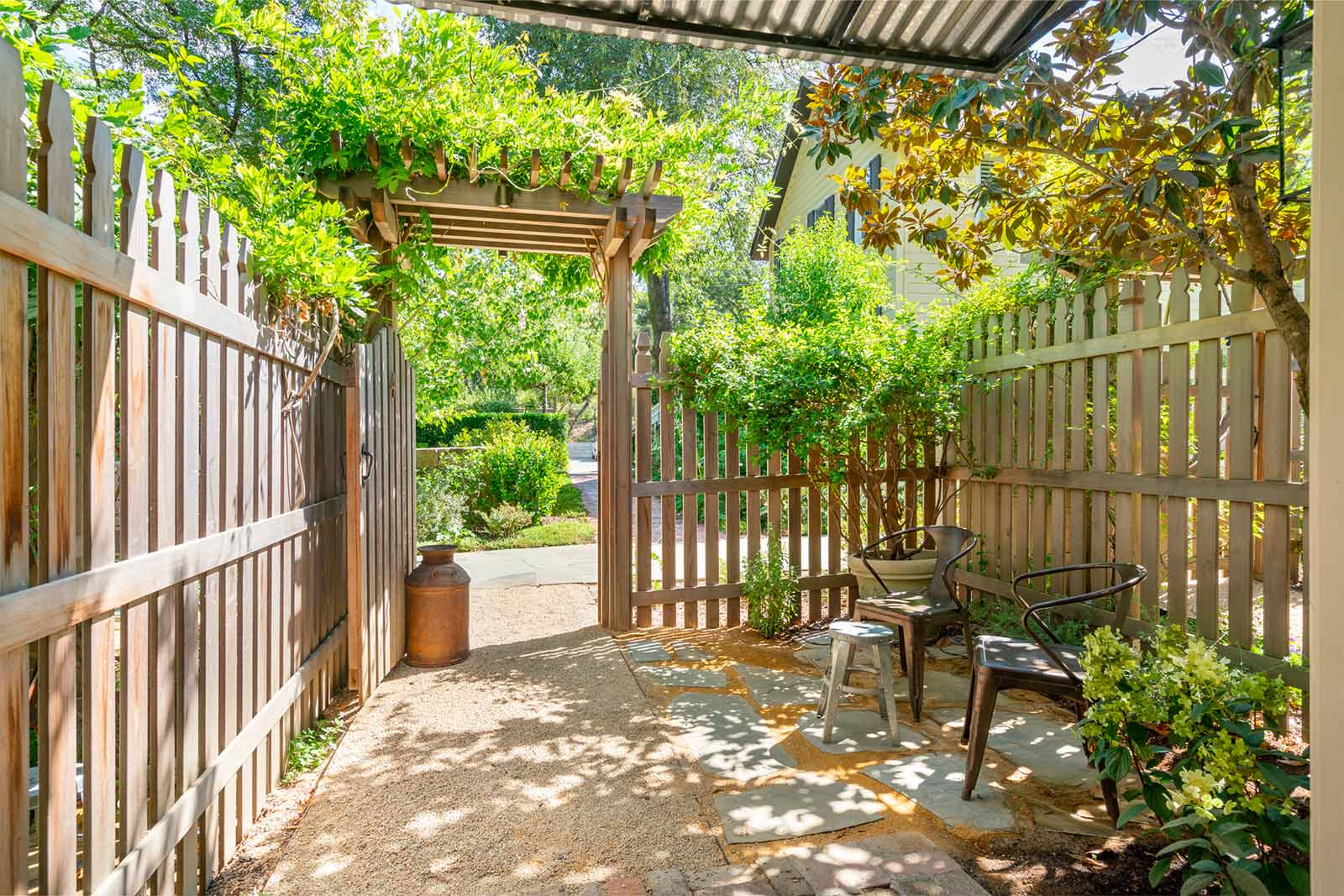 Exterior view of Cottage Room patio: tall wood picket fence with path out of a gate and lush greenery in the distance.