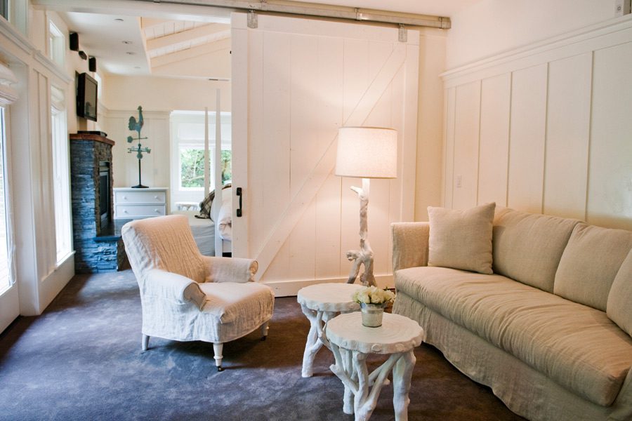 Interior of Barn One Bedroom Suite: White wood partition sliding door in back, white cushioned chair and loveseat with white corner lamp and two small coffee tables.