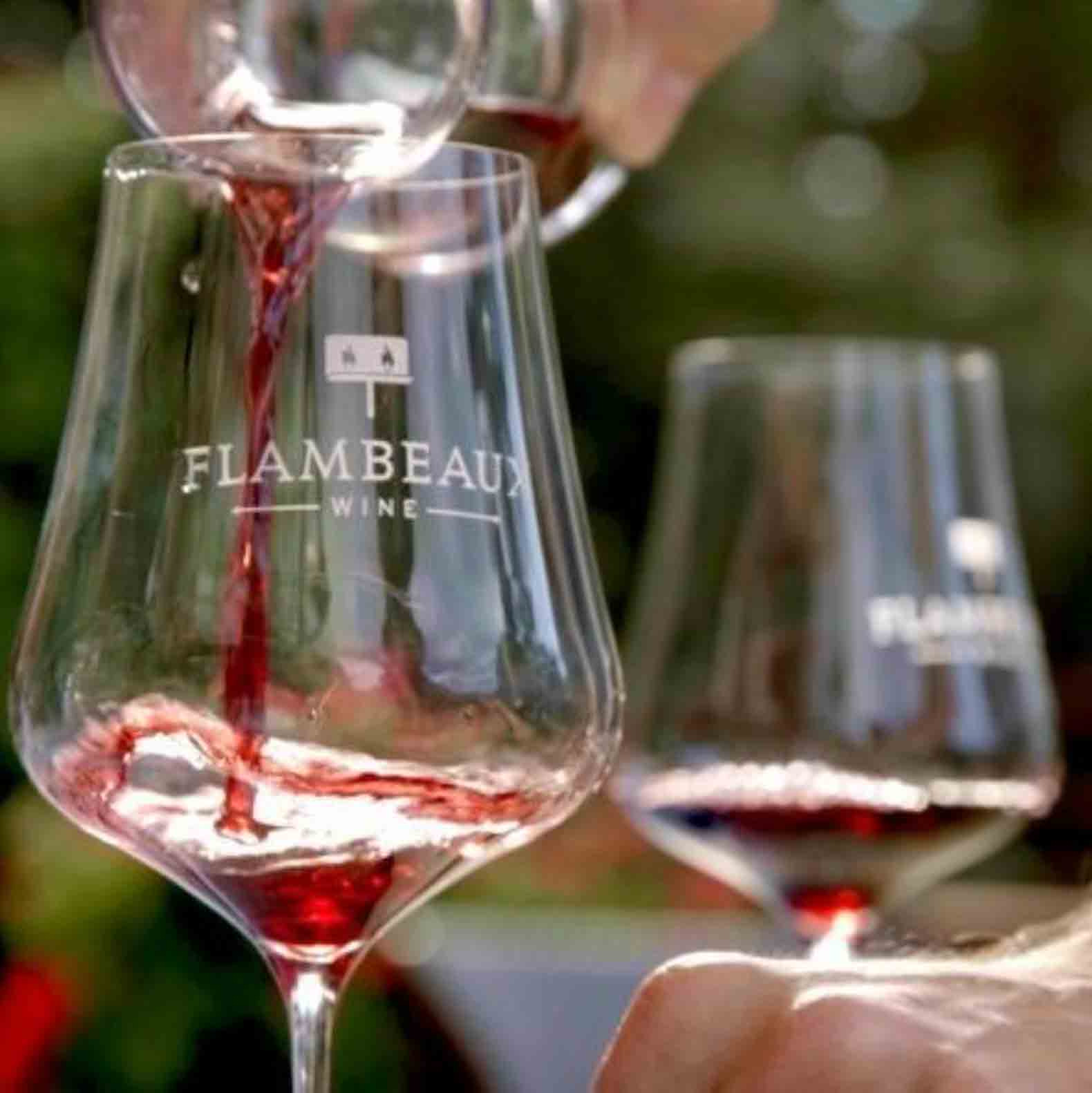 Two wine glasses with Flambeaux logo with red wine being poured in