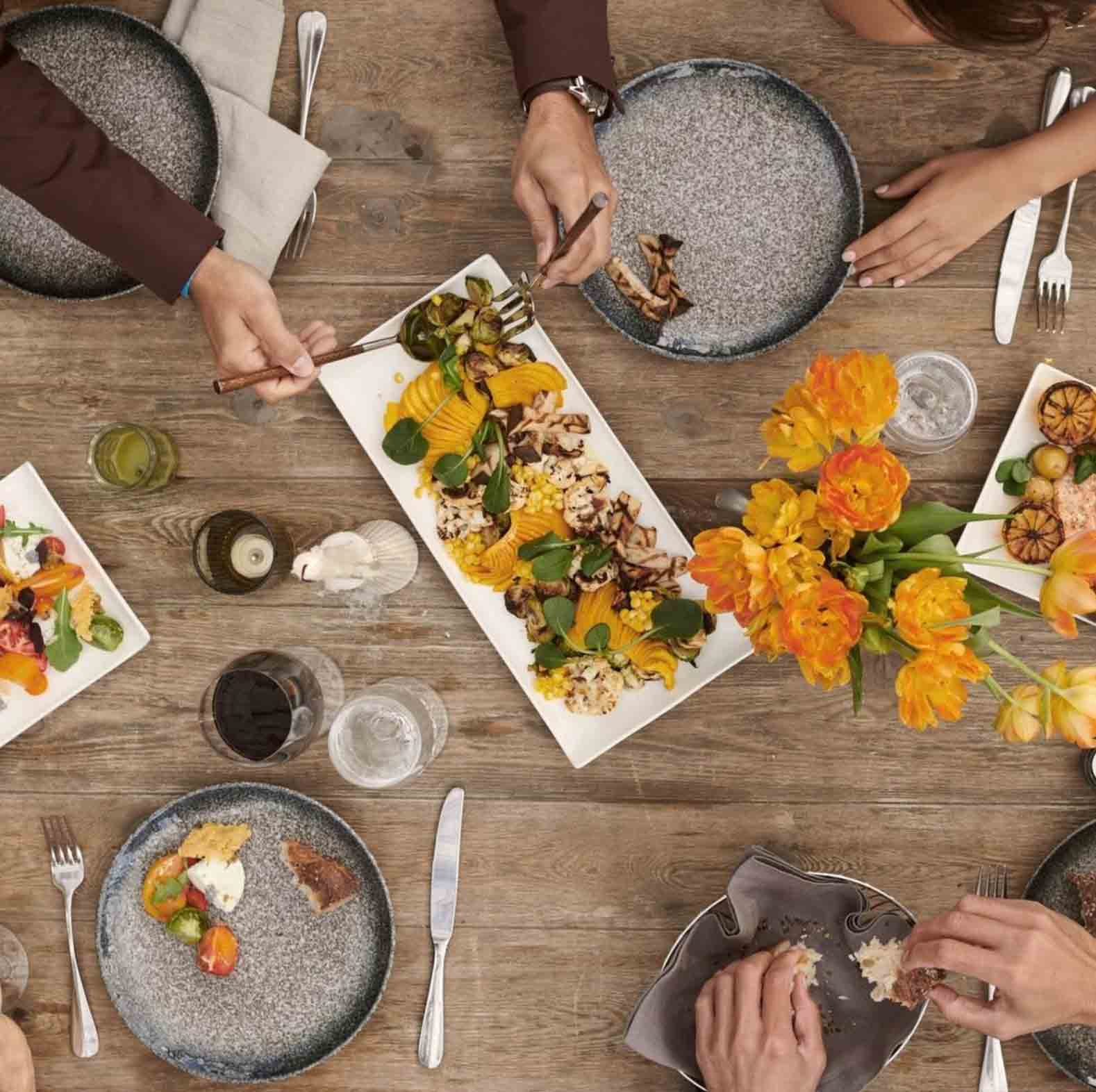 overhead view of wood table with 3 plates of appetizers and several people's place settings