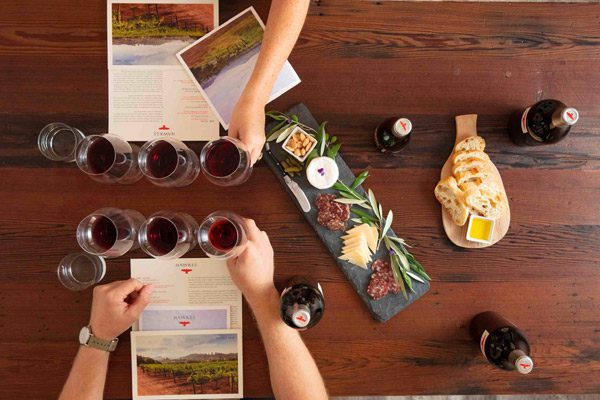 Overhead view of a wood table with several wine glasses, meat, cheese and bread platters, and menus.