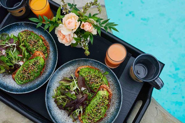 An overhead view of a dark tray with two elegantly plated salads, with flowers next to pool.