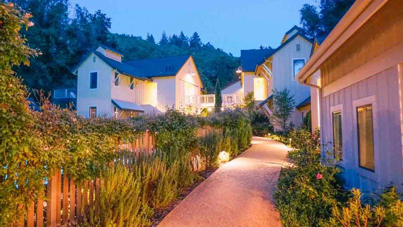 Quaint pathway on the perimeter of one of the Farmhouse Inn buildings at dusk, surrounded by lush greenery.