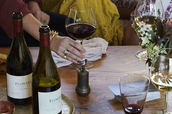 two bottles of wine on a lazy susan with three wine glasses and women drinking around a table