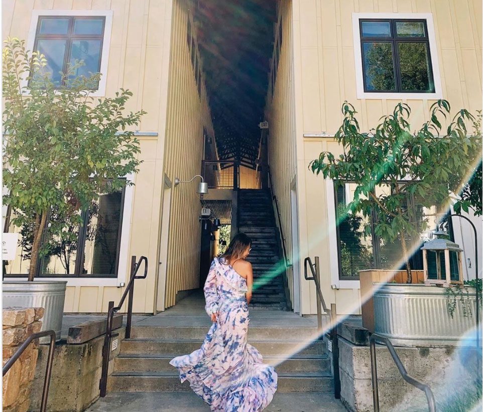 behind photo of woman in a blue and white long dress walking up steps outside at the Farmhouse Inn