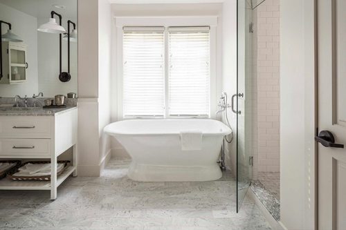 Bathroom inside the Cottage Petite Suite. white standalone bathtub, shower with glass door, light colored floor tiles, white modern vanity with two drawers and large mirror to ceiling.