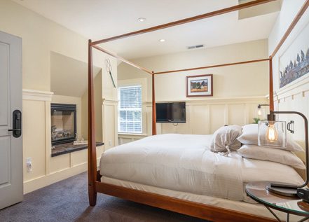 Interior of Farmhouse room: large bed with brown wood bedframe and bed posts, ornate wood moulding on walls and farmed picture on wall.