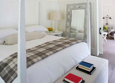 inside the Barn One Bedroom Suite showing king-sized bed with white bedding and large stand-up mirror and lamp.