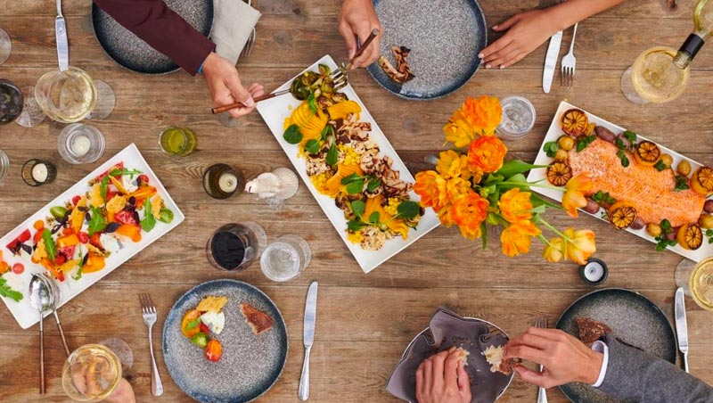 overhead view of wood table with 3 plates of appetizers and several people's place settings