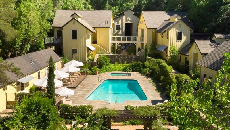 Aerial view of center of Farmhouse Inn. Yellow buildings with swimming pool in the middle and some greenery surrounding the area.