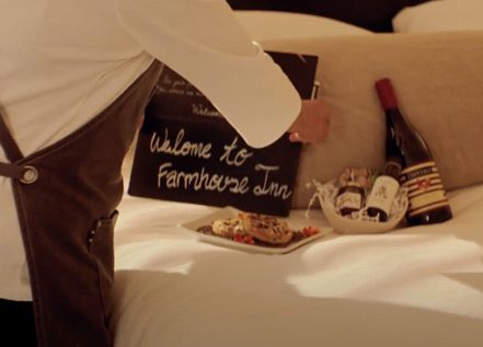 Farmhouse Inn employee preparing the welcome sign and wine and gift, on the bed in a room.