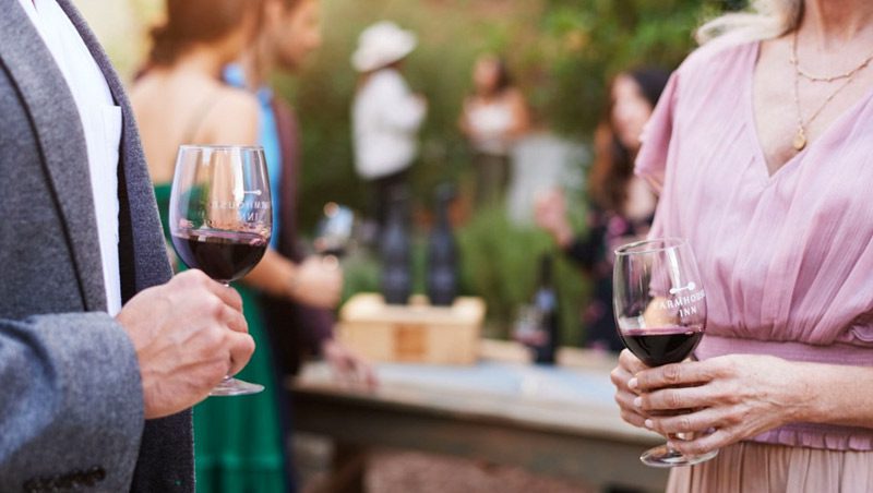 casual photo of a man and woman conversing at wine tasting, holding glasses of red wine.